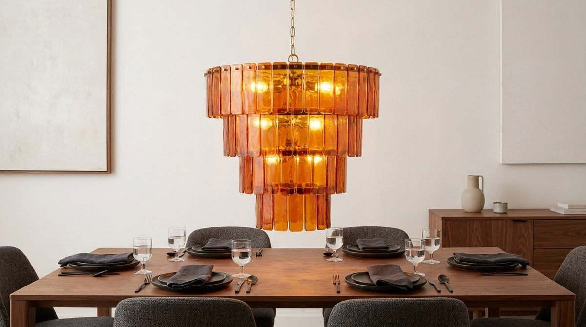 Amber glass chandelier hanging above a walnut dining table set for dinner, warm evening light