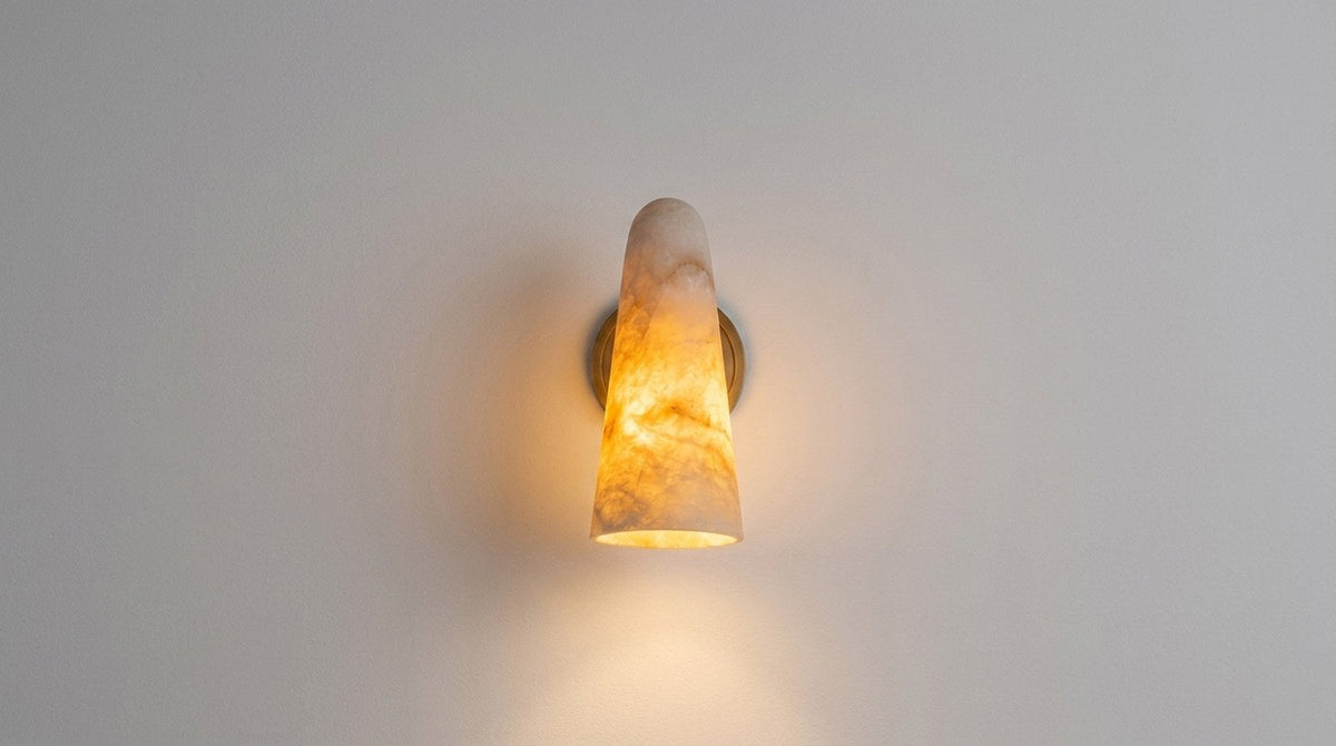 Alabaster cylinder wall sconce mounted on a plain wall, switched on and glowing softly