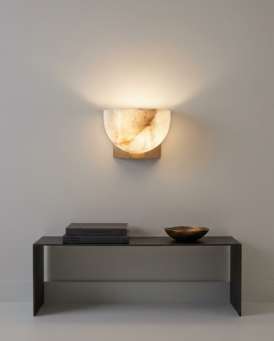 Brass and Alabaster Disc Sconce mounted on an off-white hallway wall above a low console, evening, warm pool of light on the wall