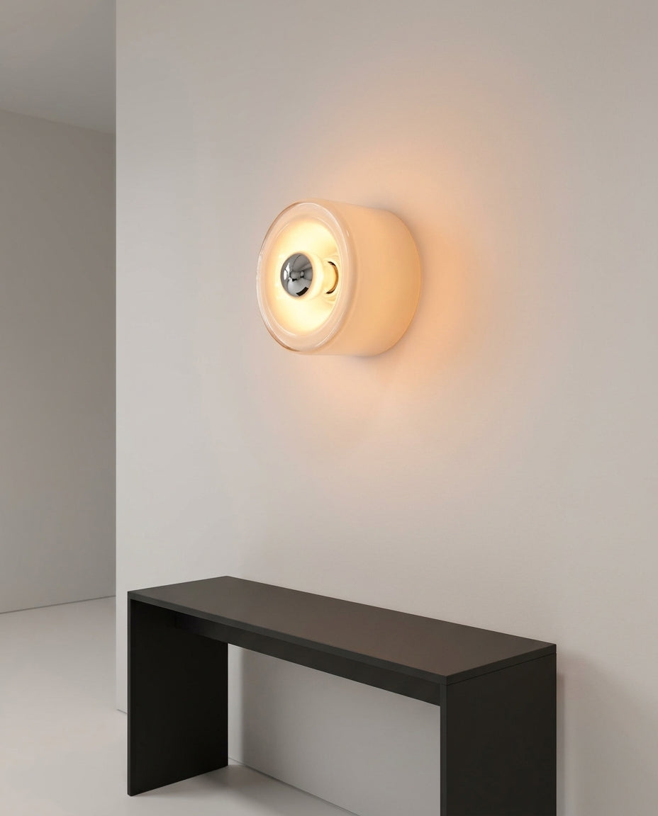 Round Glass Wall Sconce mounted on an off-white hallway wall above a low console, evening, warm pool of light on the wall