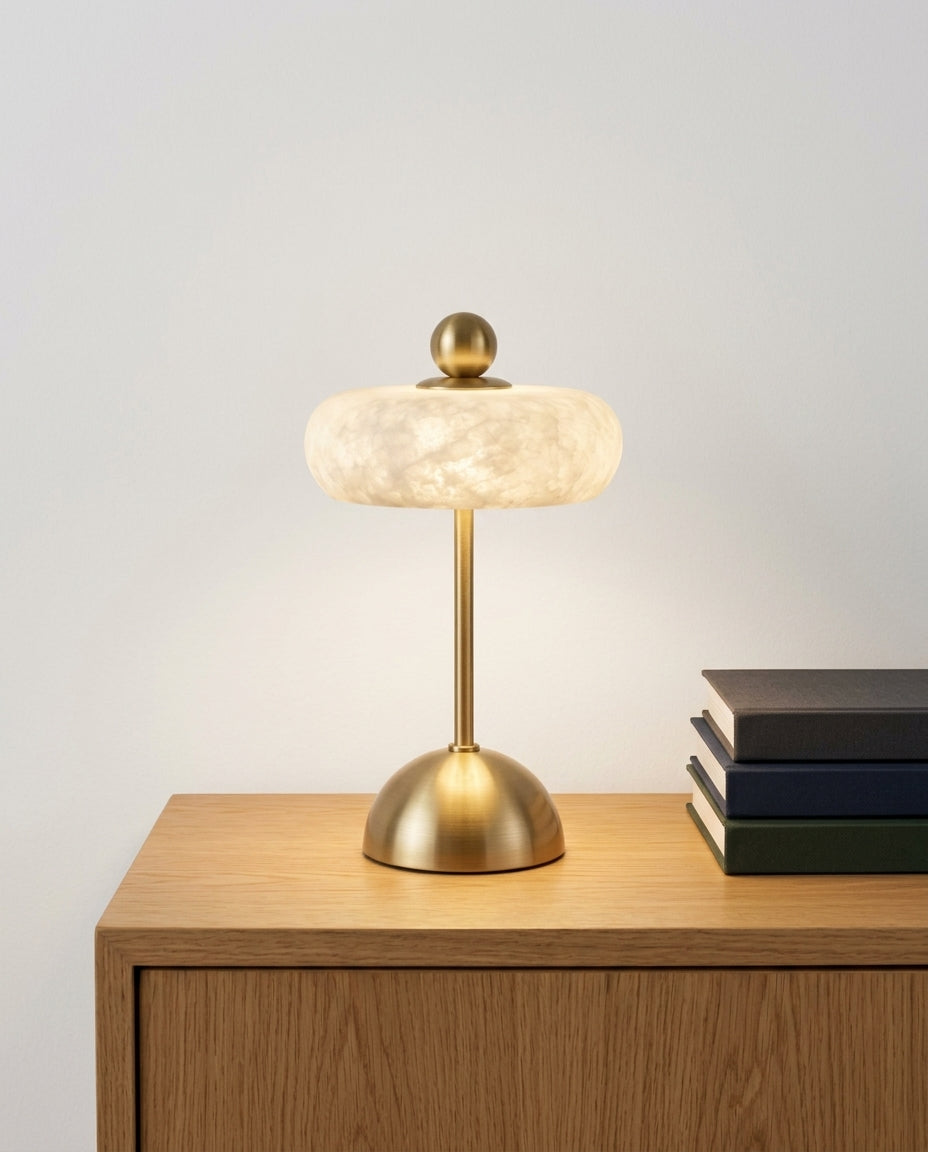 Alabaster Disc Table Lamp on an oak sideboard against an off-white wall, evening, a small stack of books beside it