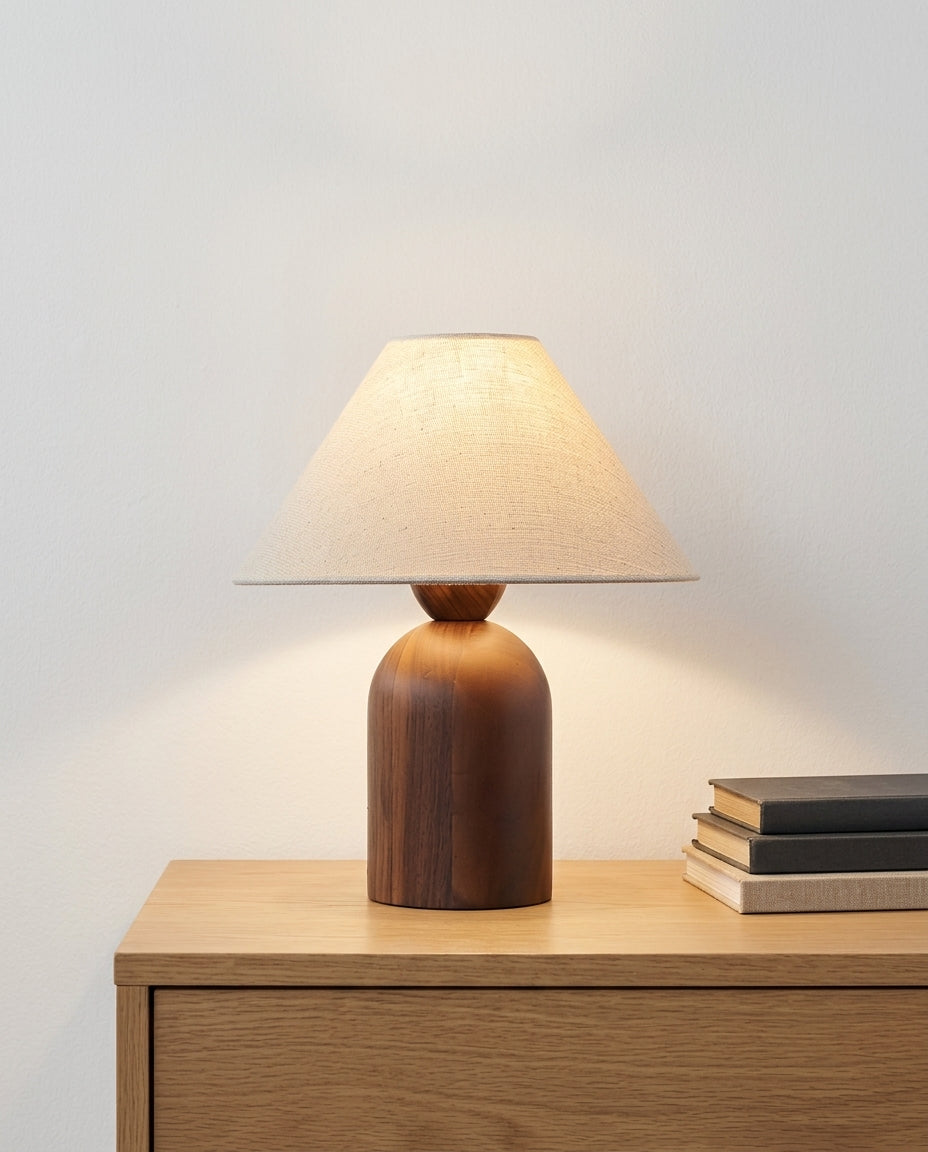 Linen and Walnut Table Lamp on an oak sideboard against an off-white wall, evening, a small stack of books beside it