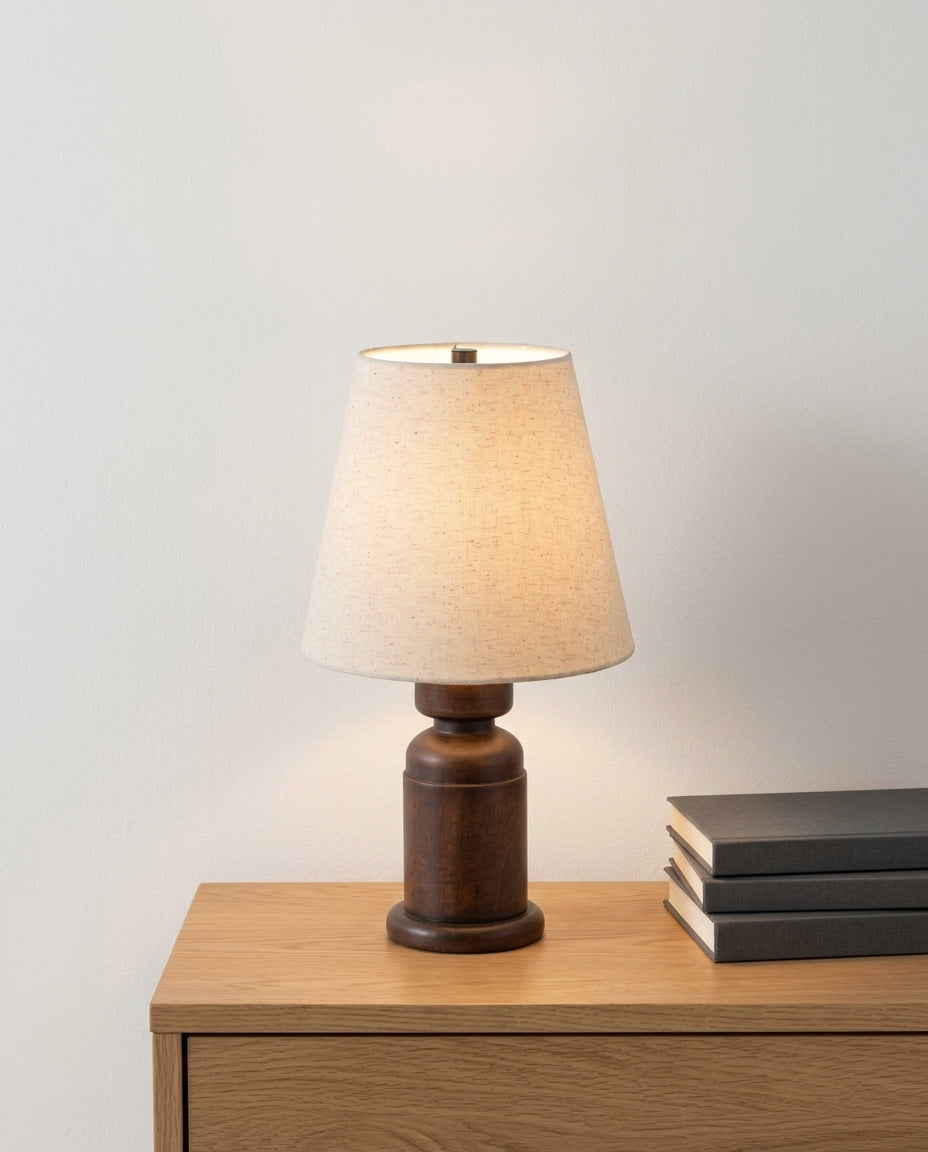 Walnut Wood Table Lamp on an oak sideboard against an off-white wall, evening, a small stack of books beside it