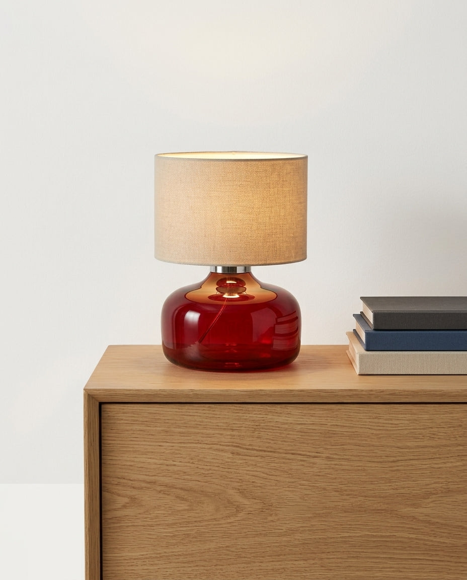 Glass and Fabric Table Lamp on an oak sideboard against an off-white wall, evening, a small stack of books beside it