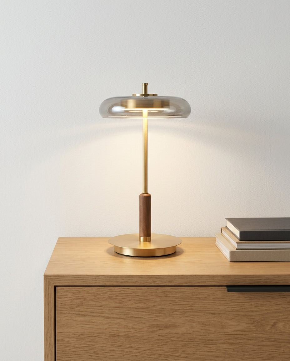 Glass, Walnut and Brass Table Lamp on an oak sideboard against an off-white wall, evening, a small stack of books beside it