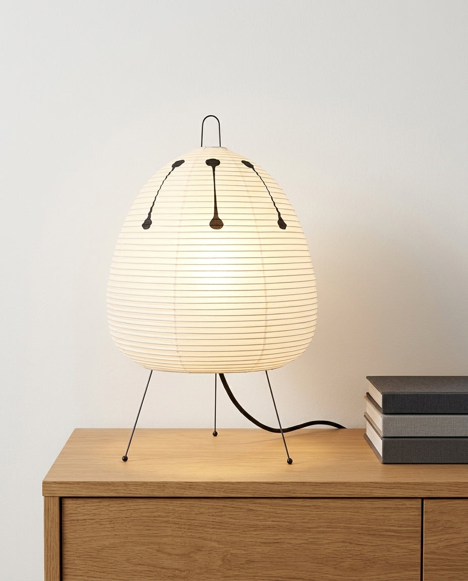 Rice Paper Tripod Table Lamp on an oak sideboard against an off-white wall, evening, a small stack of books beside it