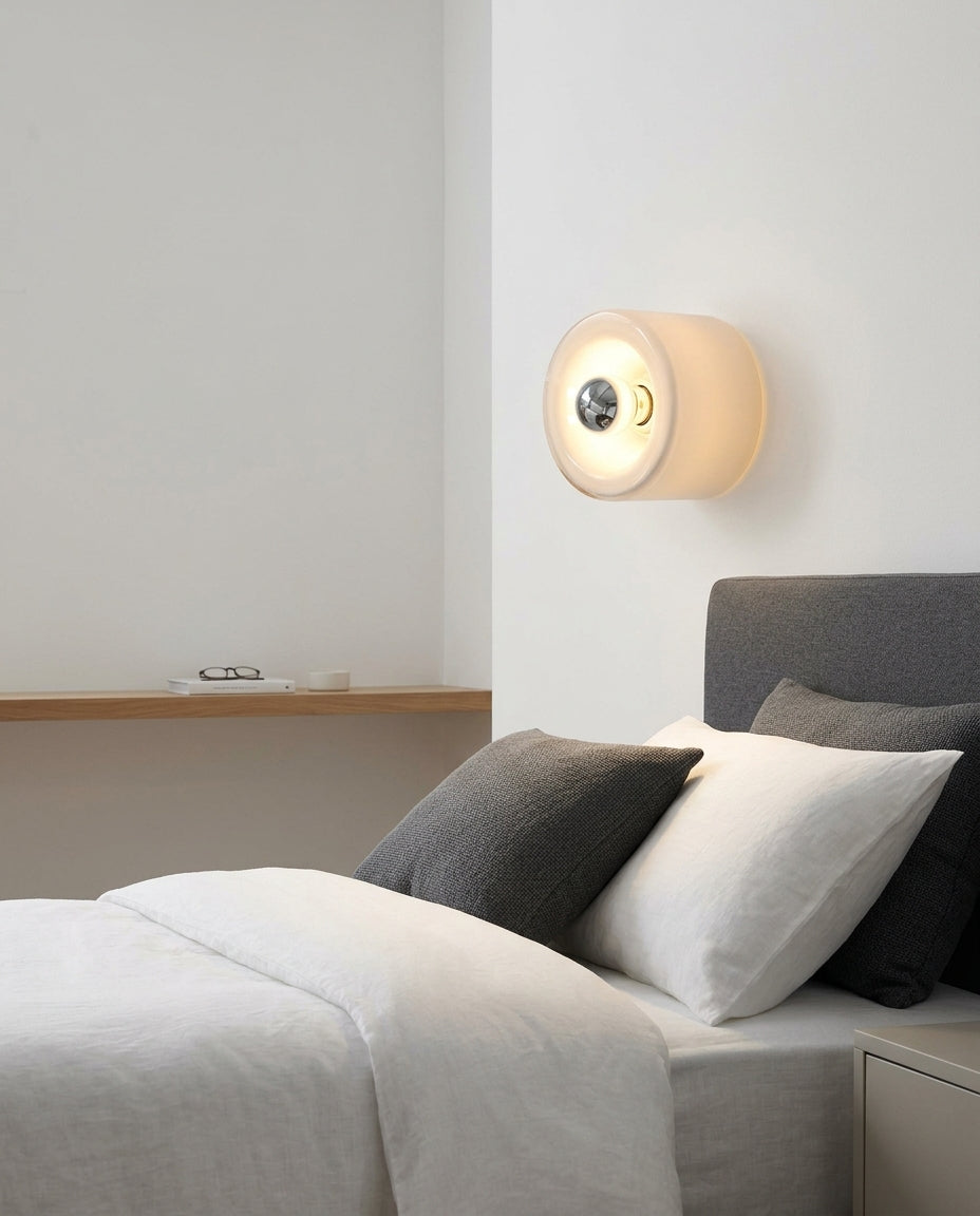 Round Glass Wall Sconce mounted on the wall beside a bed in place of a bedside lamp, reading light angled down