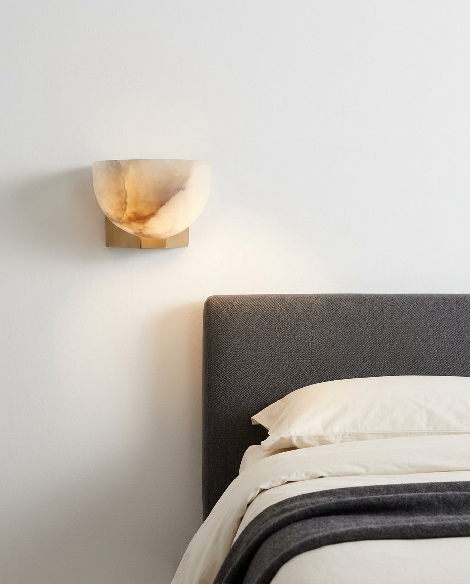 Brass and Alabaster Disc Sconce mounted on the wall beside a bed in place of a bedside lamp, reading light angled down