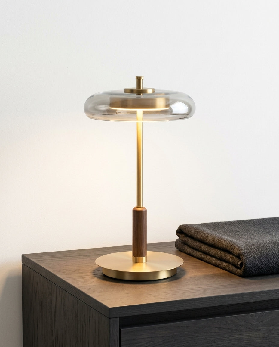 Glass, Walnut and Brass Table Lamp on a bedside table beside a folded throw, warm evening light