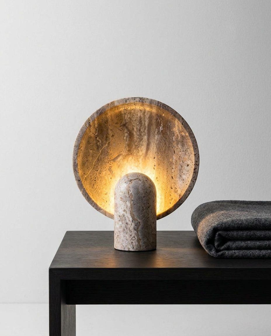 Travertine Table Lamp on a bedside table beside a folded throw, warm evening light