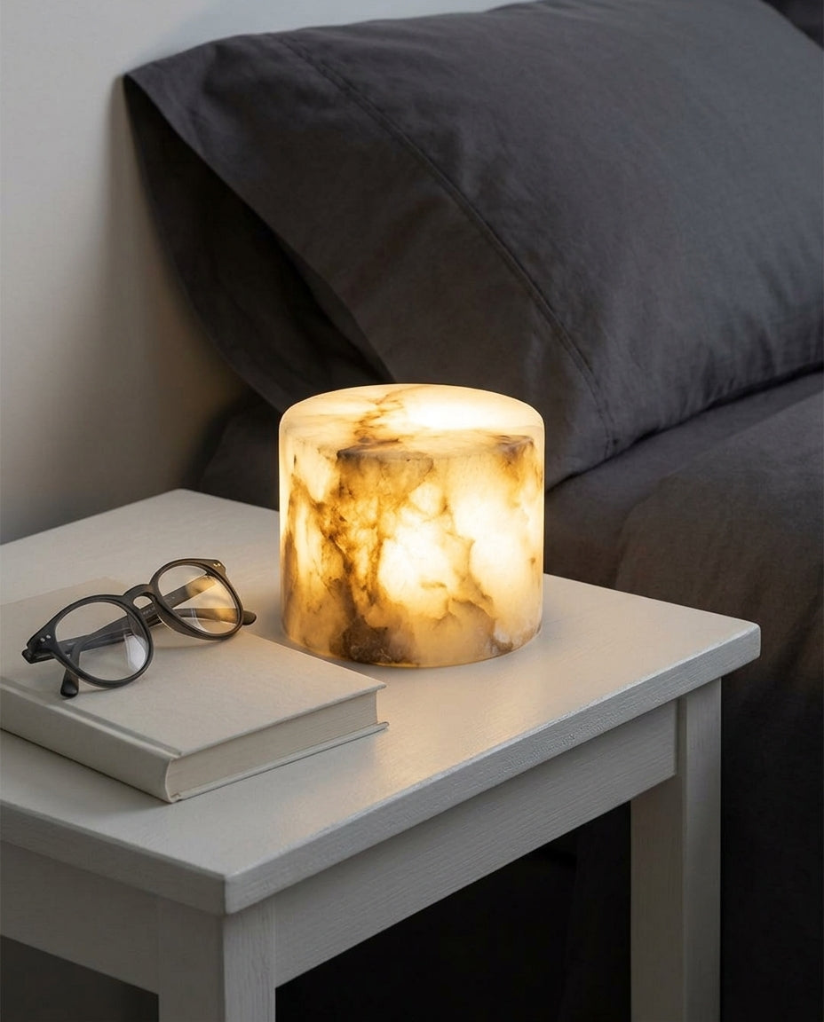 Alabaster Puck Cordless Lamp on a bedside table beside a folded throw, warm evening light