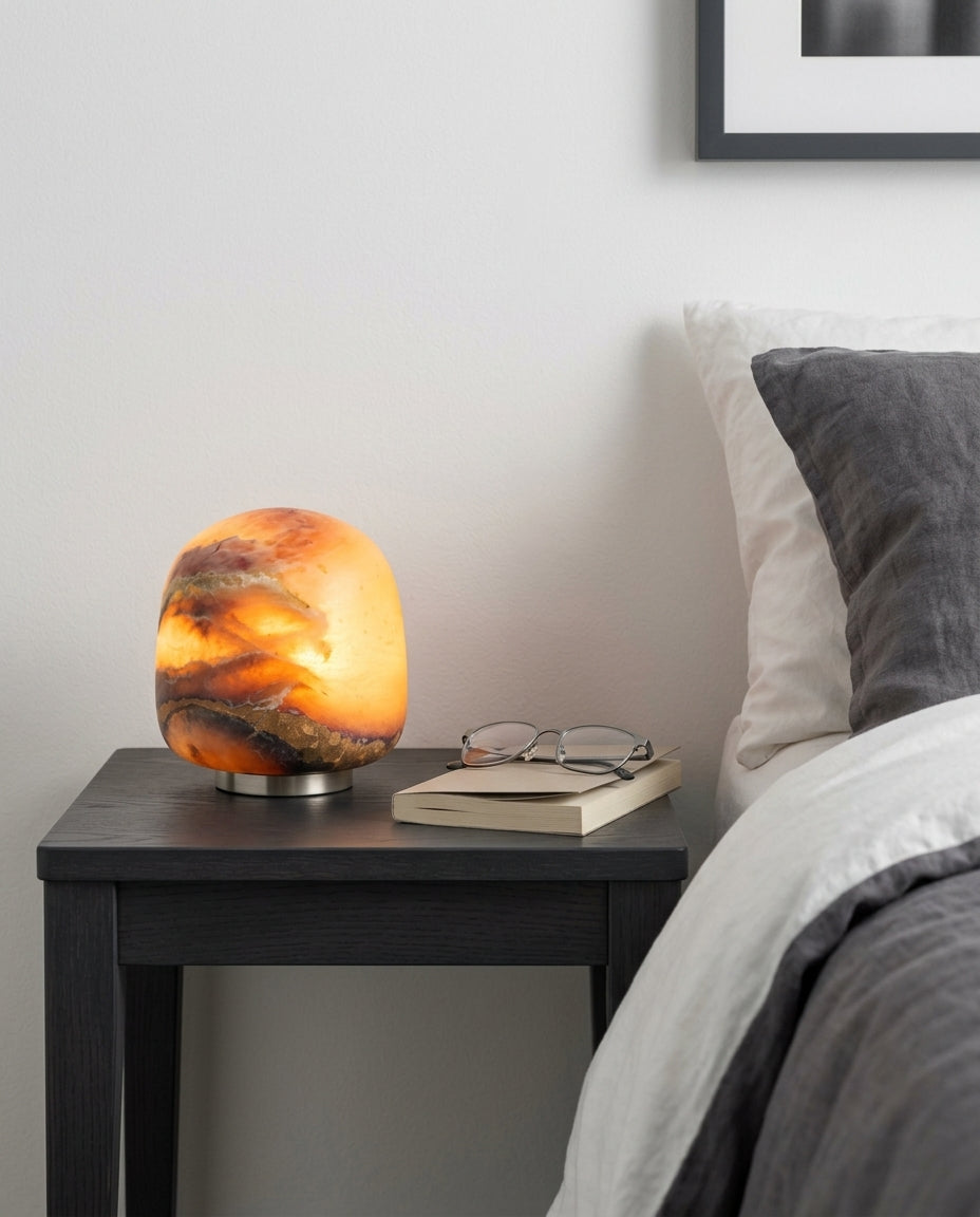 Alabaster Petite Portable Lamp on a bedside table beside a folded throw, warm evening light