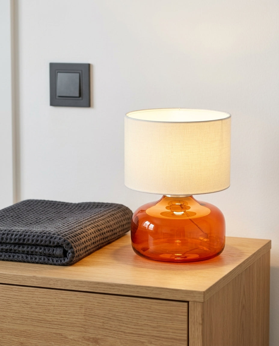 Glass and Fabric Table Lamp on a bedside table beside a folded throw, warm evening light