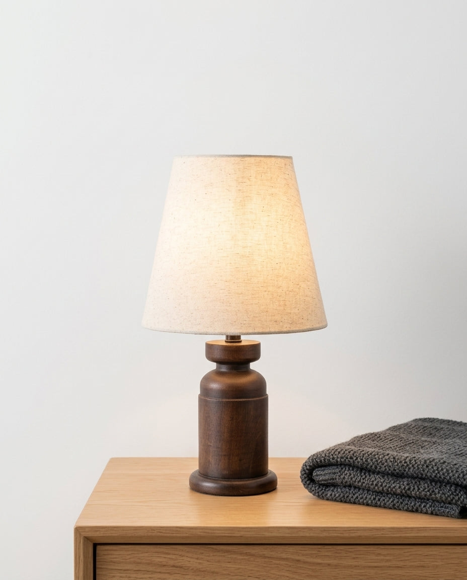 Walnut Wood Table Lamp on a bedside table beside a folded throw, warm evening light