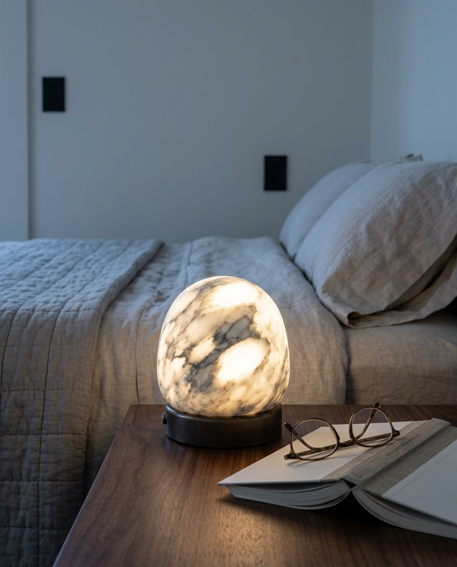 Alabaster Dome Cordless Lamp on a bedside table beside a folded throw, warm evening light