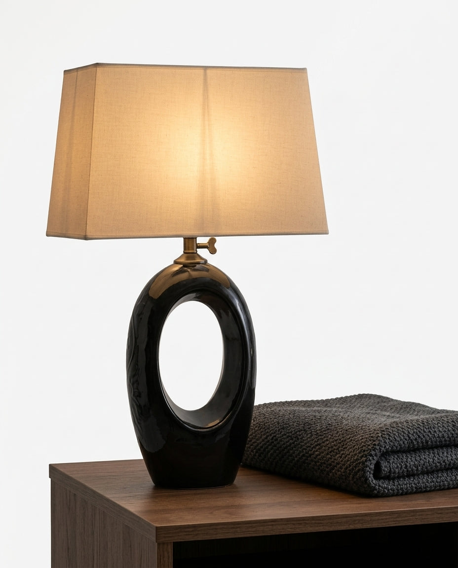 Ceramic and Fabric Table Lamp on a bedside table beside a folded throw, warm evening light