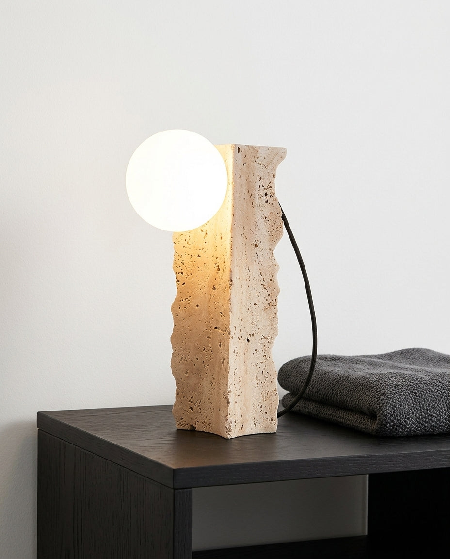 Travertine Column Table Lamp on a bedside table beside a folded throw, warm evening light