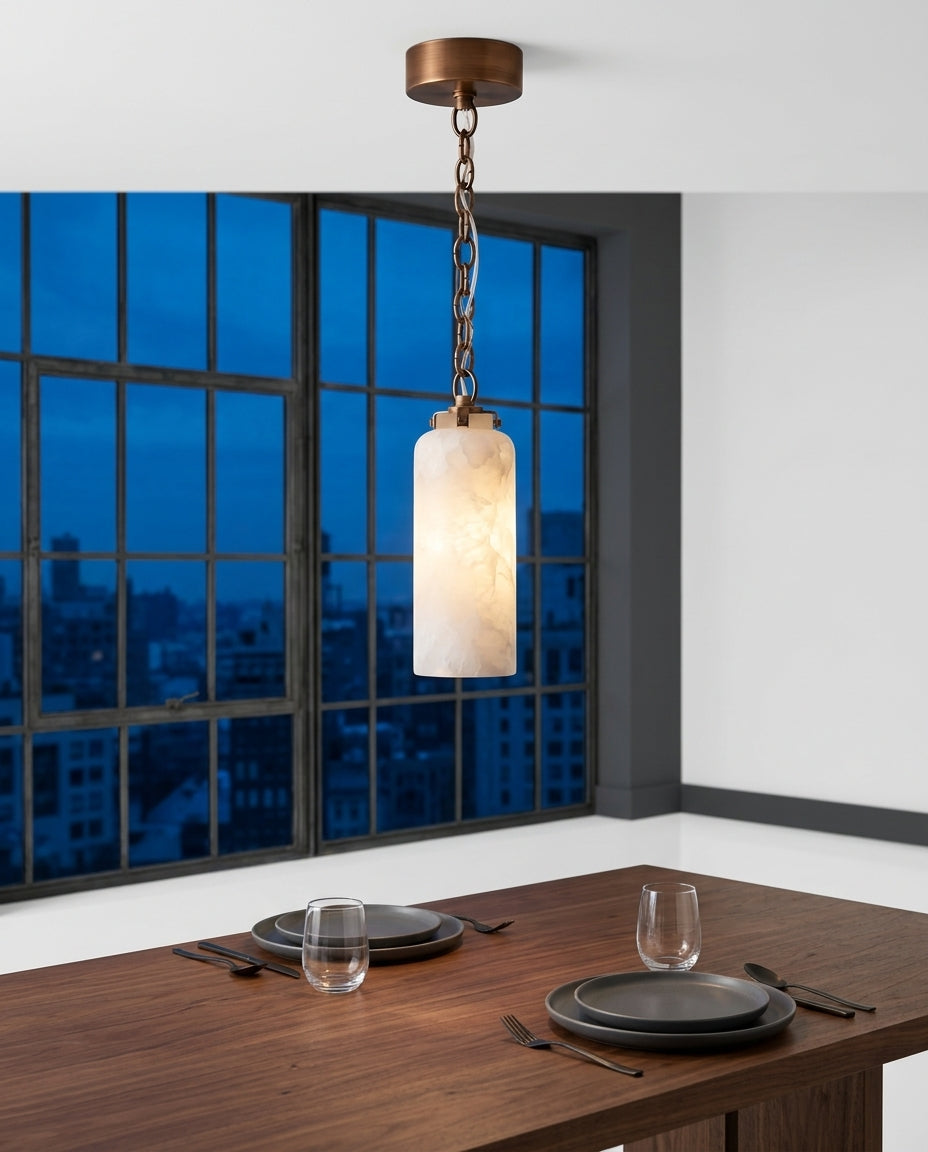 Slim Alabaster and Brass Pendant Light hanging above a walnut dining table set for two, blue-hour light through a large window